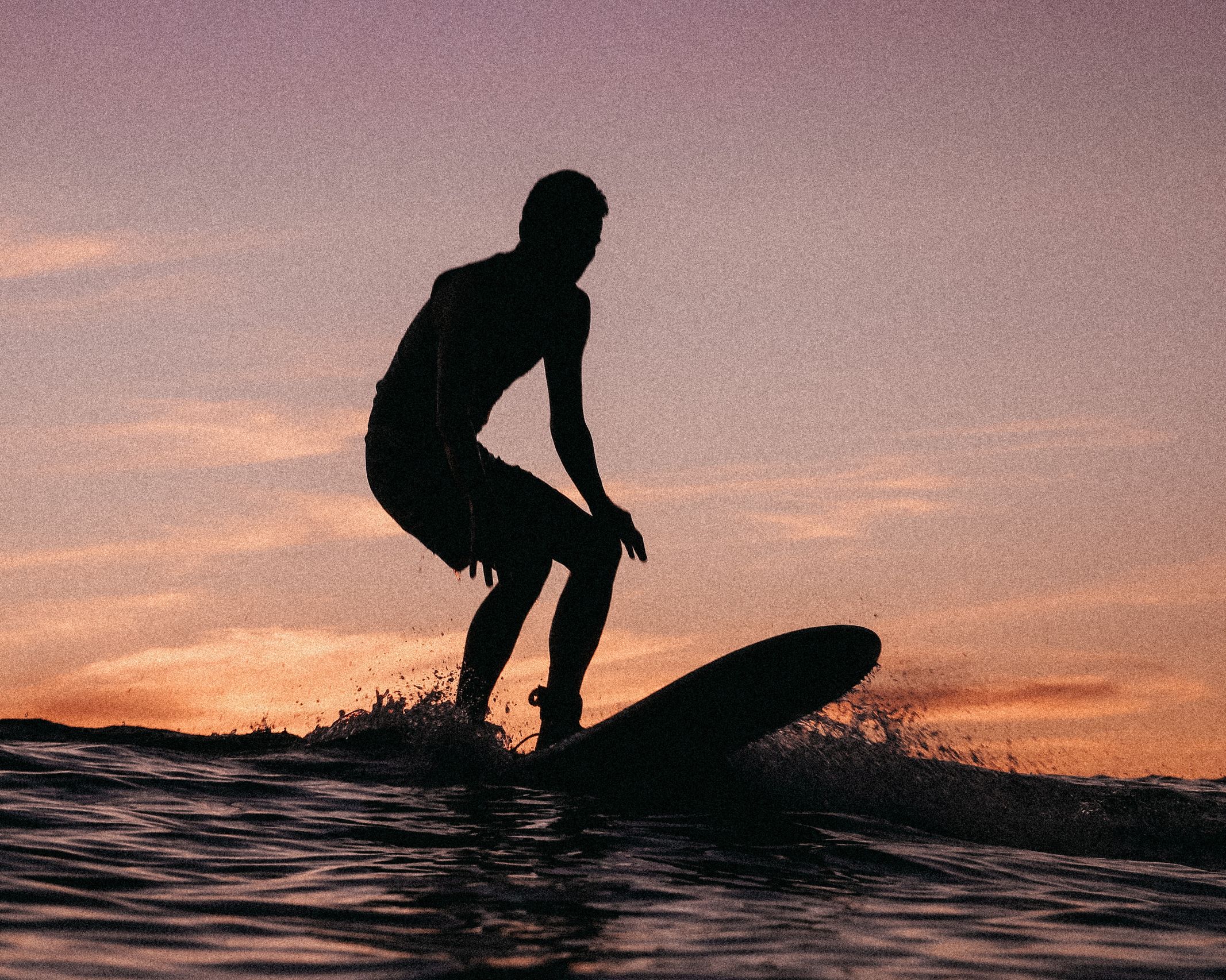 Surfer riding wave at sunrise